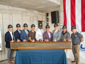 Nine men signing a steel beam as a celebratory gesture for completing the last floor of LRC Construction's New Rochelle residential tower.