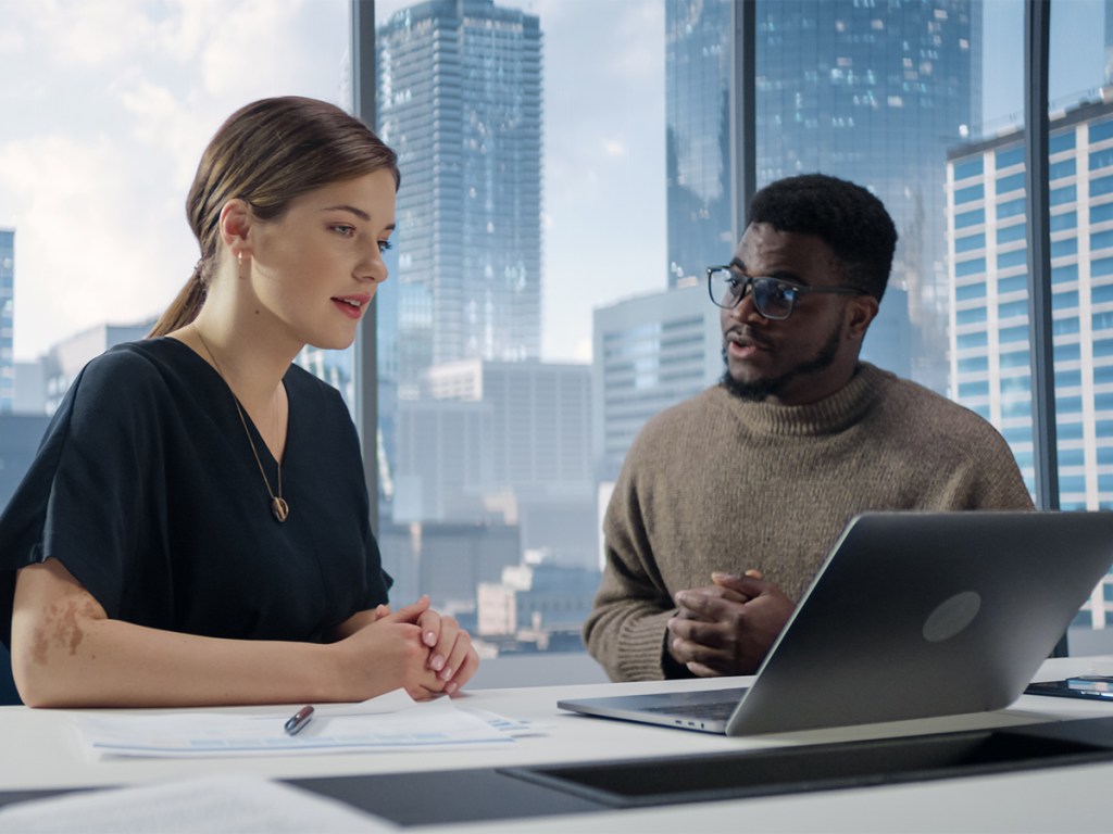 Businesspeople in Modern Office: Business Meeting of Two Managers Using Laptop. Female CEO and African American Operations Director Discuss Strategy, Implementing Financial Plans.