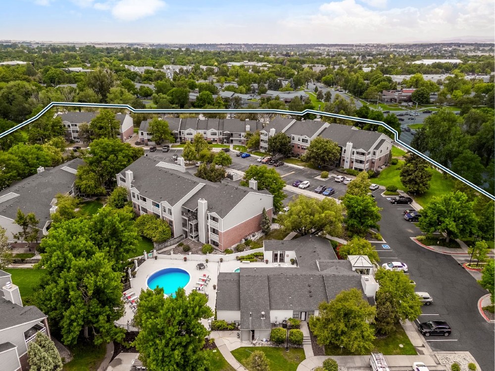  Aerial view of Courtney Park, a garden-style community with gray and brown buildings, surrounded by trees. The picture also shows the property’s swimming pool in the center.