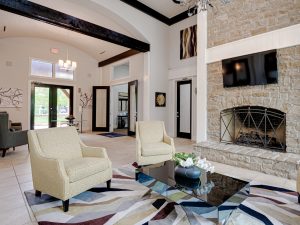 Interior shot of the clubroom at The Brazos property, under LUMA Residential management. The room includes two white chairs, a coffee table and a tv on the wall
