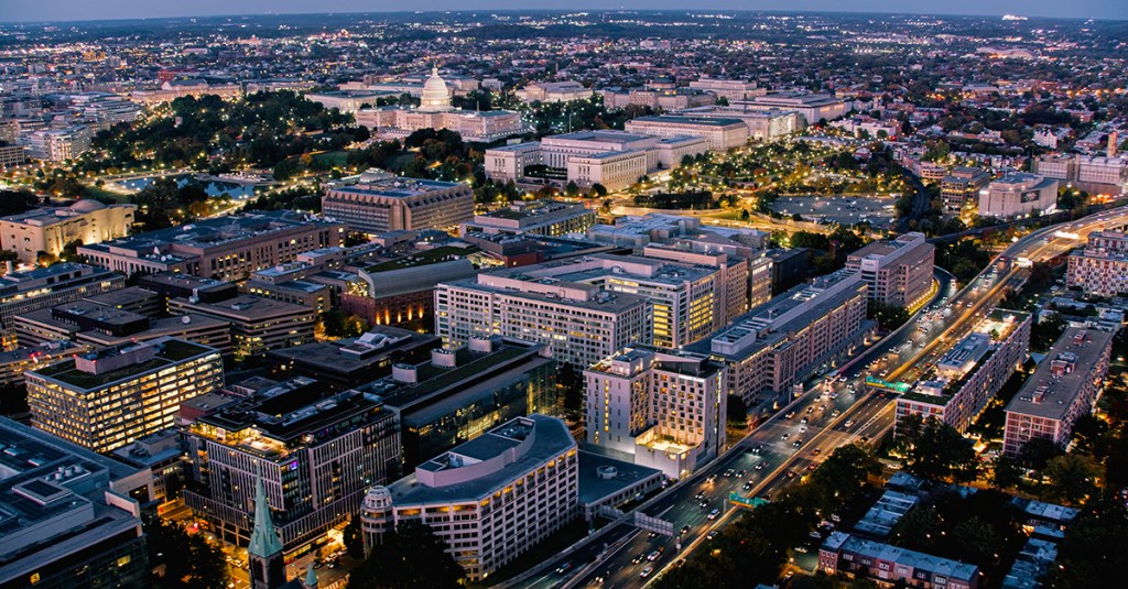 Helicopter shot of Washington, D.C. at twilight on a clear evening in Fall, looking down on office buildings to the south of the Capitol Building and National Mall and traffic on the Southeast Freeway.