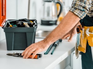 Cropped image of plumber putting tools on kitchen counter in kitchen