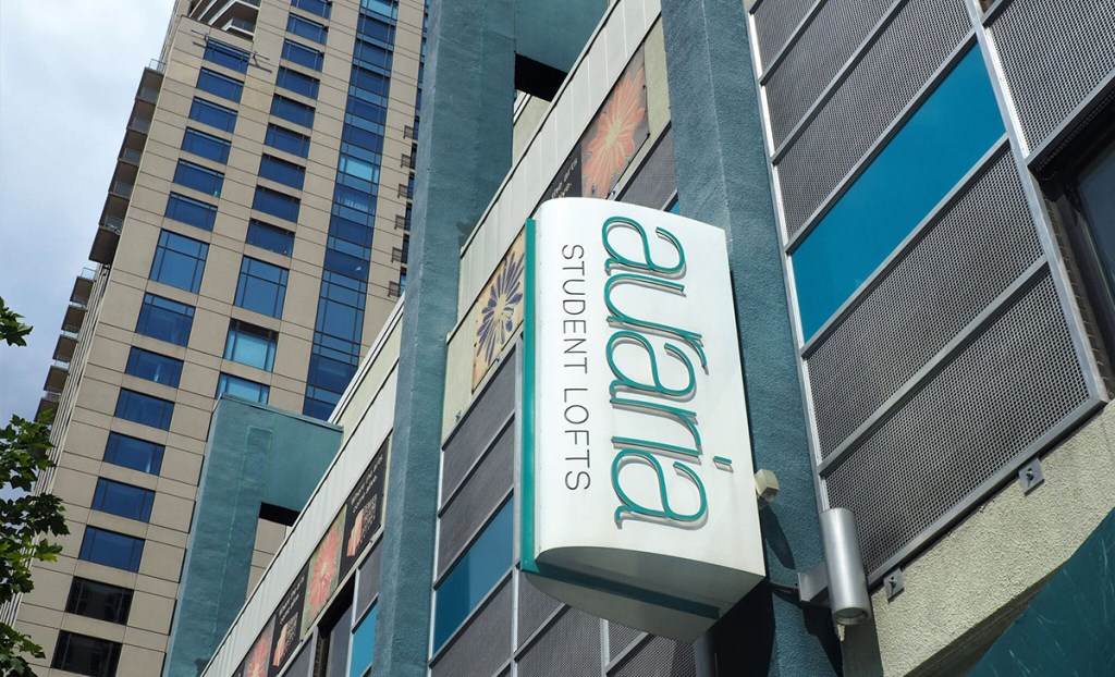 Exterior view of Auraria Student Lofts, a high-rise student housing community in Denver, with a large vertical sign saying Auraria Student Lofts. 
