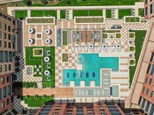 Aerial view of apartment community pool flaked by a deck, deck chairs and mid-rise sections of a apartment building on three sides