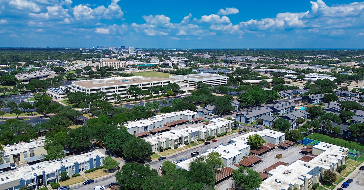 Blending of low rise flat roofed apartment complexes, multilevel parking structure from corporate campus, office buildings, major highways, and distant skyline background in Richardson, Texas. USA