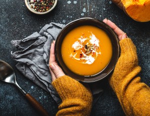 Woman in a sweater holding pumpkin soup.