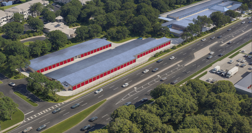 exterior shot of self storage property in Hudson, Fla., under the ownership of Hearthfire Holdings. Image features an overhead shot of storage facilities with red and blue doors near a roadside, surrounded by trees