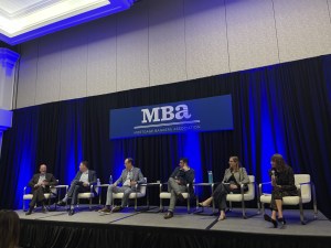A photo of Stephanie Wiggins, managing director & head of production and agency lending at PGIM leading a panel discussion with Sheri Thompson of Walker & Dunlop, Phil Maniscalco of Wells Fargo, Bill Buskirk of Freddie Mac, Chuck Walker of Fannie Mae and the MBA's Jamie Woodwell.