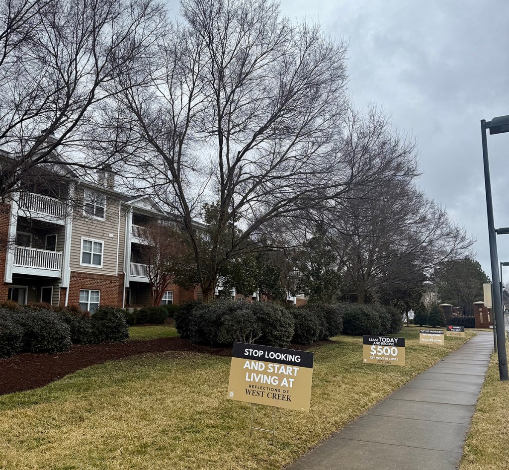 A photograph of an apartment community with signs along the sidewalk advertising the apartments.