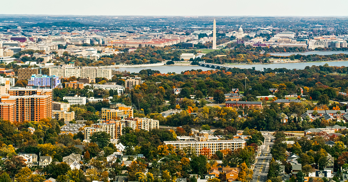 Helicopter shot of Washington, D.C. on a hazy afternoon in Fall from over Arlington, VA, looking across the city towards the Washington Monument and the Capitol Building.