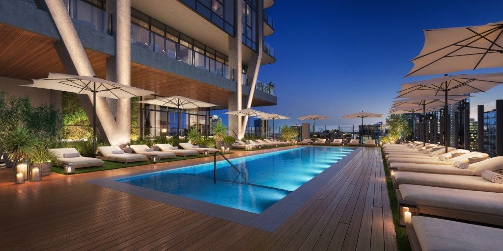 Rooftop pool at dusk with a serene atmosphere. Surrounded by plush lounge chairs, umbrellas, and soft lighting, set against a modern building.