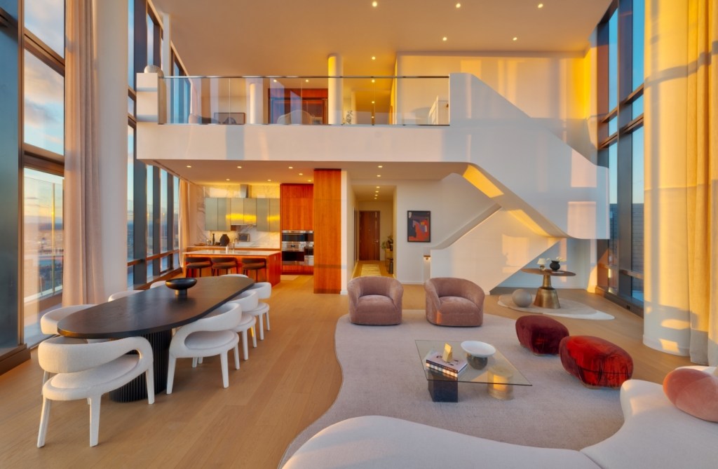Luxurious, sunlit duplex with floor-to-ceiling windows, stylish furniture, open kitchen, and modern staircase. Warm, inviting ambiance with sunset hues.