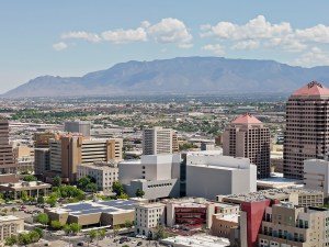 Aerial shot of downtown Albuquerque, New Mexico, with Sandia Crest visible in the distance, on a sunny day. * Authorization was obtained from the FAA for this operation in restricted airspace.