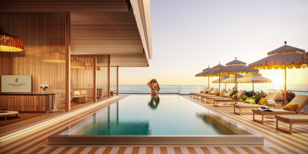 Luxurious rooftop pool at sunset with striped deck, yellow sun umbrellas, and plush loungers. The serene setting overlooks a tranquil ocean view.