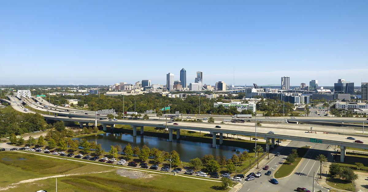 Aerial view of Jacksonville city with high office buildings and american freeway intersection with fast moving cars and trucks. USA transportation infrastructure concept.