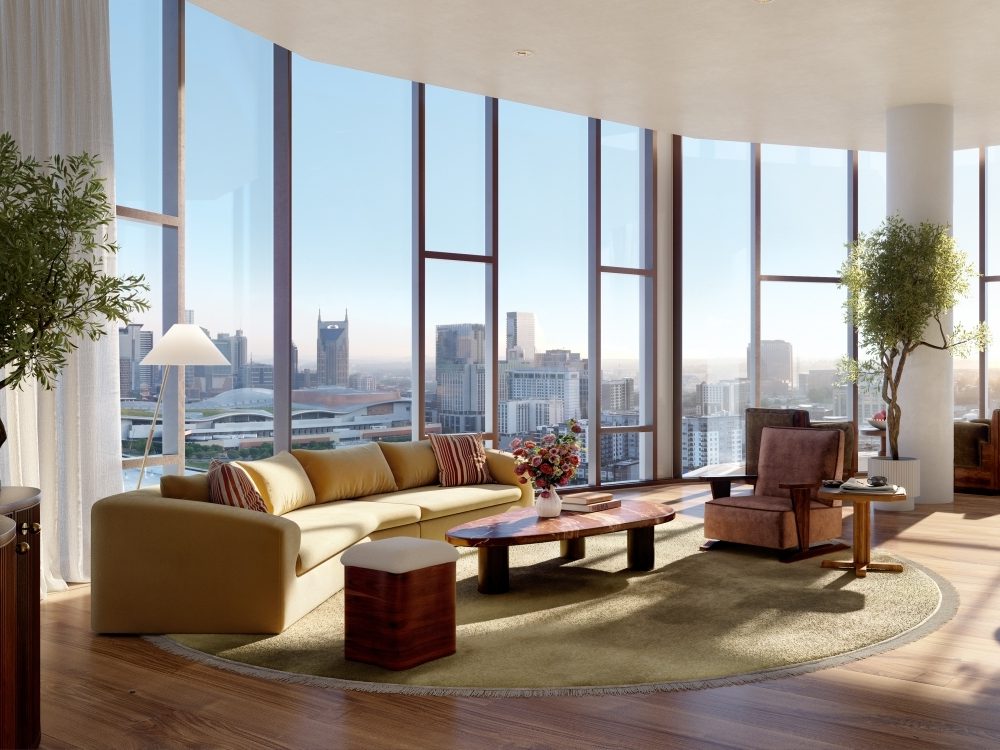 Luxurious living room with floor-to-ceiling windows offering a city skyline view. Features a beige sofa, wooden coffee table, plants, and warm lighting.