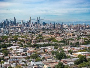Aerial view of Manhattan midtown highlighting the tall slender Billionaires Row skyscrapers. Queens and Long Island City are in the foreground with many low rise buildings and trees.