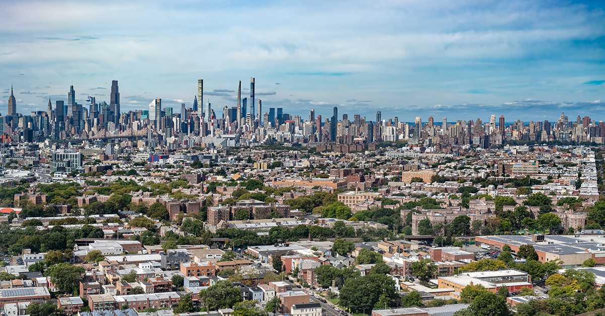 Aerial view of Manhattan midtown highlighting the tall slender Billionaires Row skyscrapers. Queens and Long Island City are in the foreground with many low rise buildings and trees.