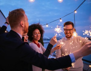 Group of people holding sparklers on a rooftop.