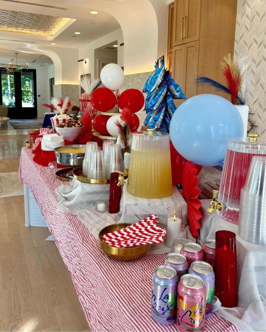 Red, white and blue event table with drinks, popcorn and snacks set up in an apartment community common area.