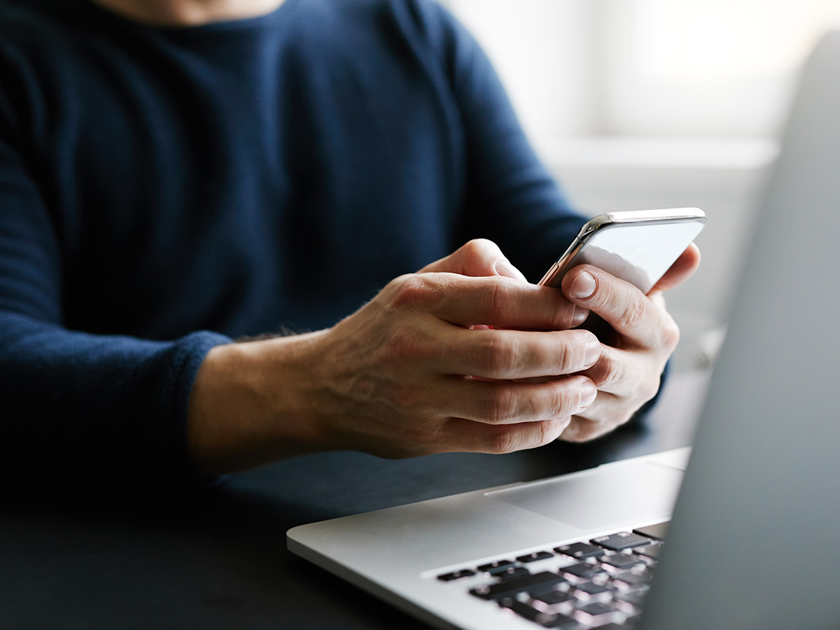 Person on phone in front of a laptop.