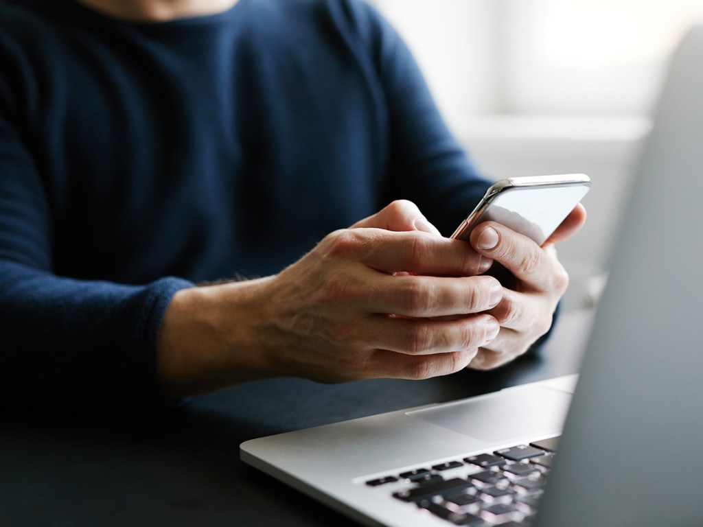 Person on phone in front of a laptop.