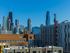 Tall buildings make up the skyline of Chicago. The scene shows a mix of architecture against a clear blue sky on a sunny day. The urban area has both new and old structures.