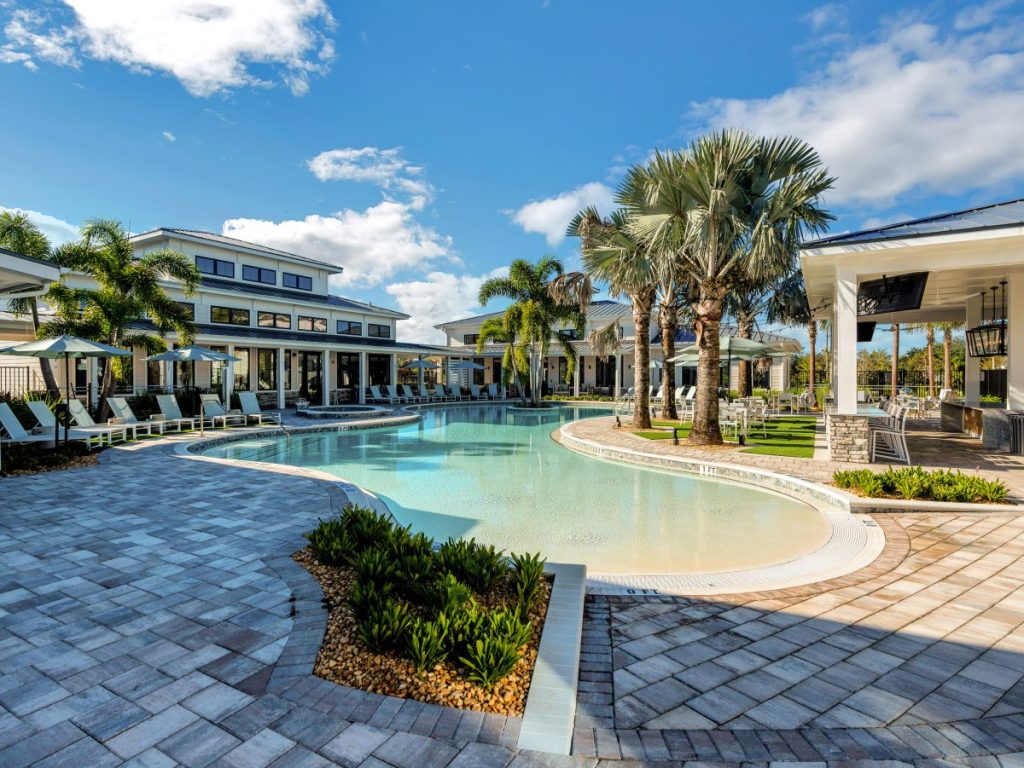 Exterior shot of Drift, a Thompson Thrift community in Daytona Beach, Fla. The image features a swimming pool surrounded by palm trees, with buildings on each side