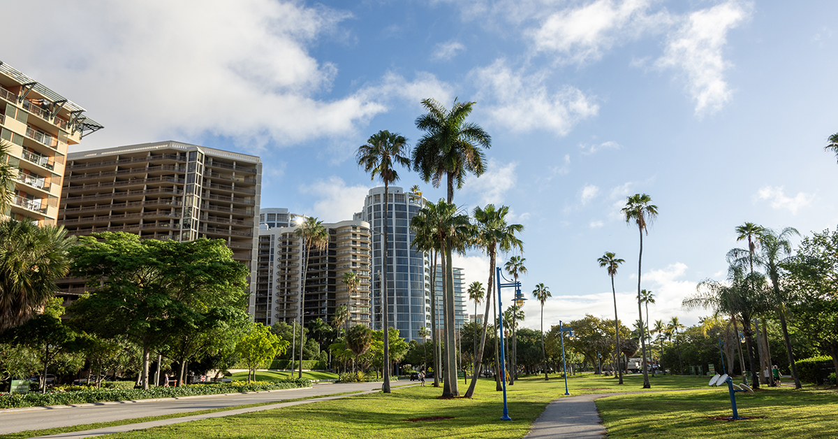 Scenic walking path through a lush tropical park surrounded by palm trees and modern skyscrapers in Coconut Grove, Miami. A peaceful urban retreat combining tropical greenery with city living.