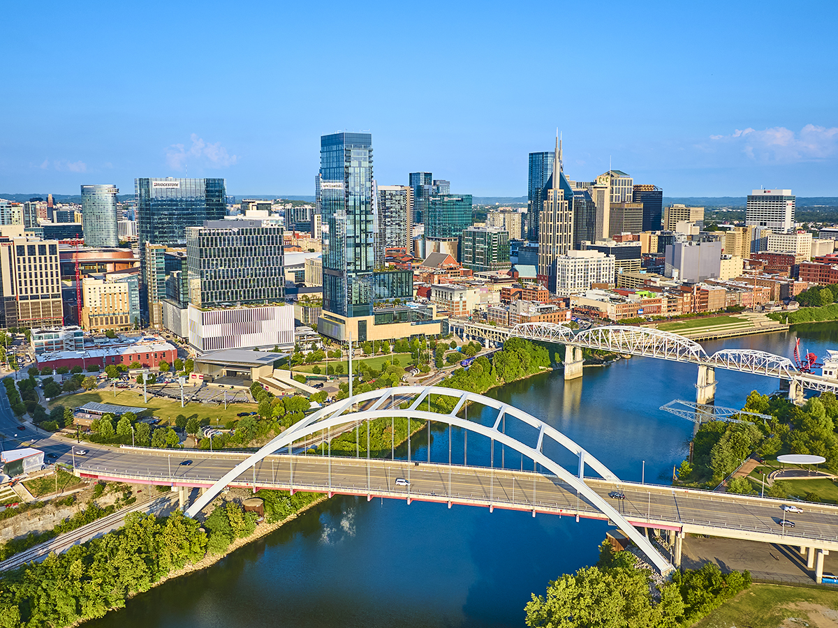Aerial view of Nashville vibrant skyline featuring modern skyscrapers and historic architecture. The iconic John Seigenthaler and Korean Veterans Memorial Bridges span the reflective Cumberland River.