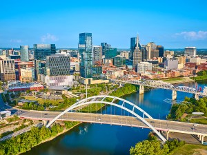 Aerial view of Nashville vibrant skyline featuring modern skyscrapers and historic architecture. The iconic John Seigenthaler and Korean Veterans Memorial Bridges span the reflective Cumberland River.
