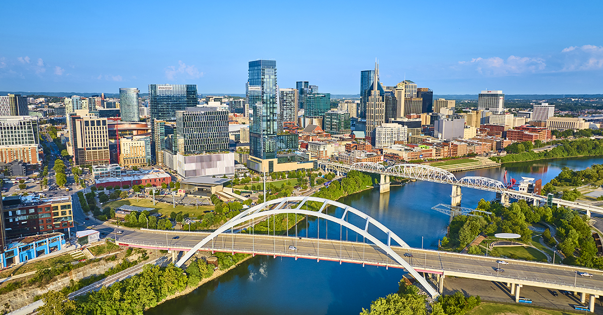 Aerial view of Nashville vibrant skyline featuring modern skyscrapers and historic architecture. The iconic John Seigenthaler and Korean Veterans Memorial Bridges span the reflective Cumberland River.