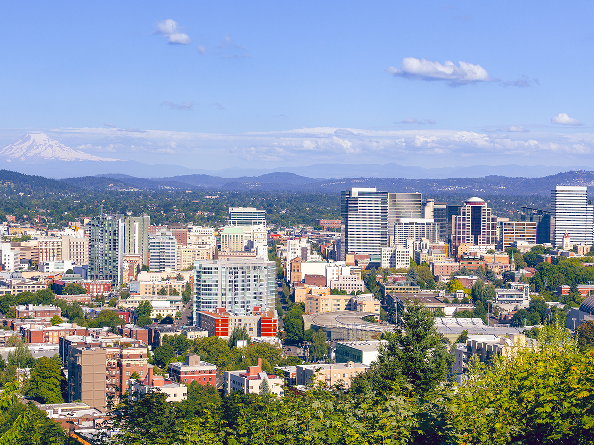 Portland's dense urban skyline nestled among lush greenery, with the snow-capped peak of Mount Hood looming majestically on the clear blue horizon.