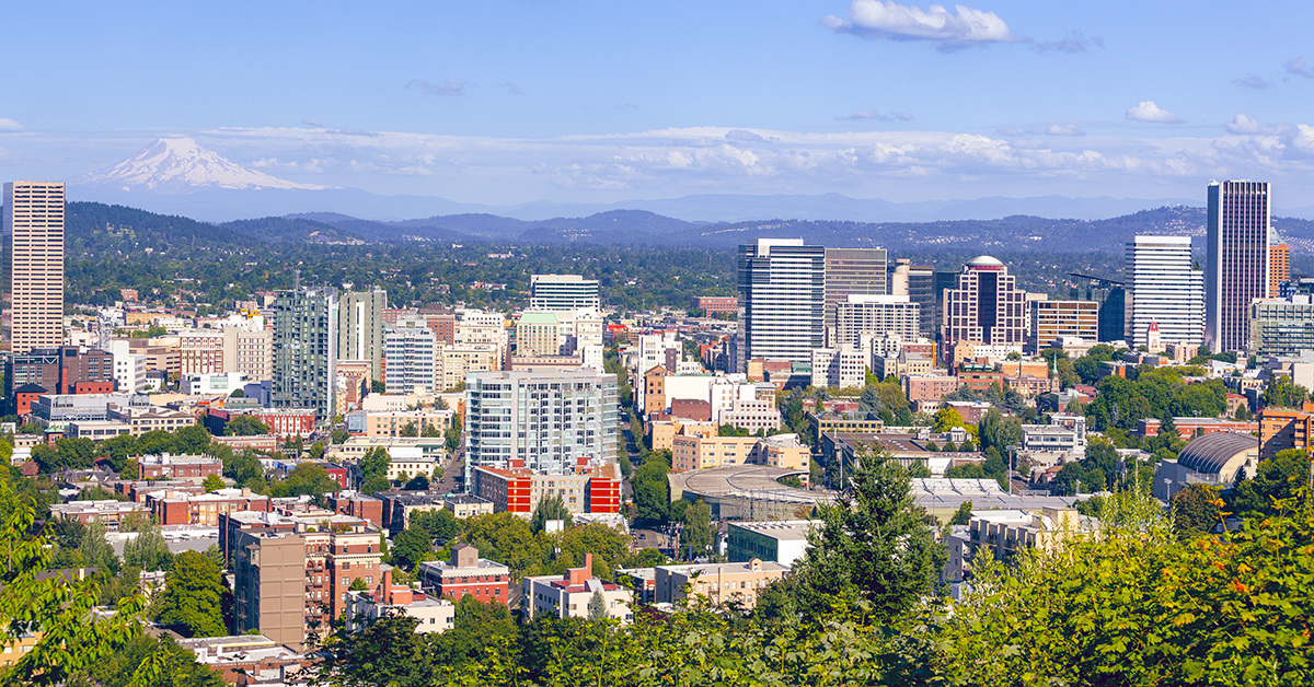 Portland's dense urban skyline nestled among lush greenery, with the snow-capped peak of Mount Hood looming majestically on the clear blue horizon.