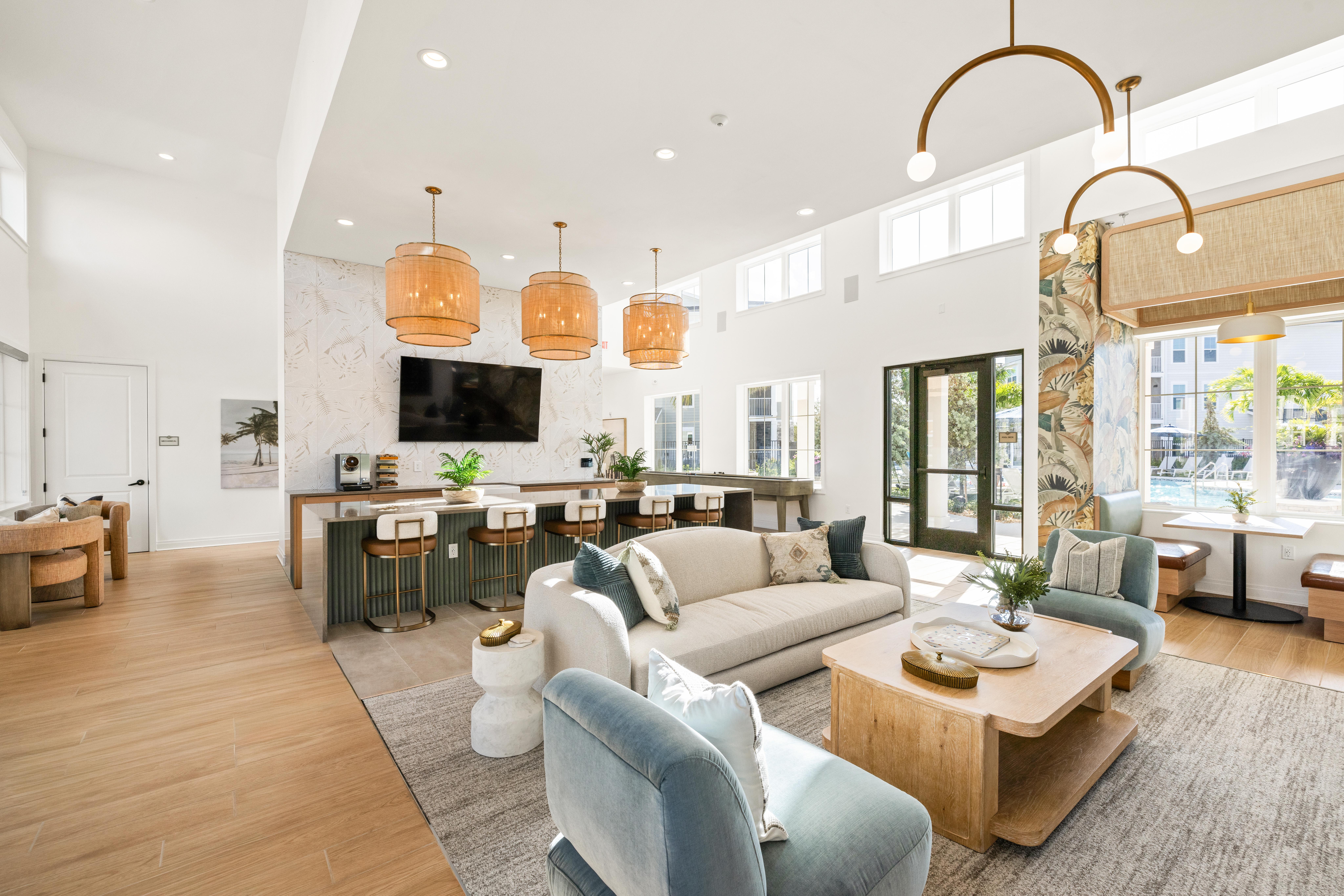 Interior shot of a communal area at Verity, a Thompson Thrift property in Vero Beach, Fla. The image features a bar, sofas and a coffee table and a tv mounted on the wall.