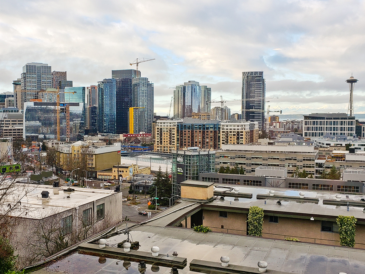 Wide panoramic view of downtown Seattle, Washington featuring the iconic Space Needle, modern skyscrapers, active construction cranes, and expanding urban development beneath a dramatic cloudy sky. Urban architecture, business district, real estate growth, and Pacific Northwest cityscape concept.