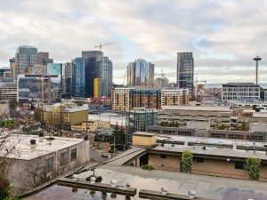 Wide panoramic view of downtown Seattle, Washington featuring the iconic Space Needle, modern skyscrapers, active construction cranes, and expanding urban development beneath a dramatic cloudy sky. Urban architecture, business district, real estate growth, and Pacific Northwest cityscape concept.