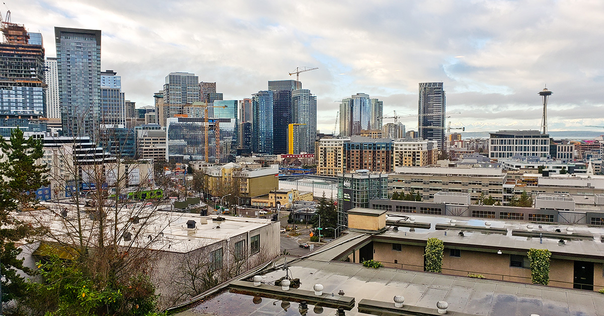 Wide panoramic view of downtown Seattle, Washington featuring the iconic Space Needle, modern skyscrapers, active construction cranes, and expanding urban development beneath a dramatic cloudy sky. Urban architecture, business district, real estate growth, and Pacific Northwest cityscape concept.