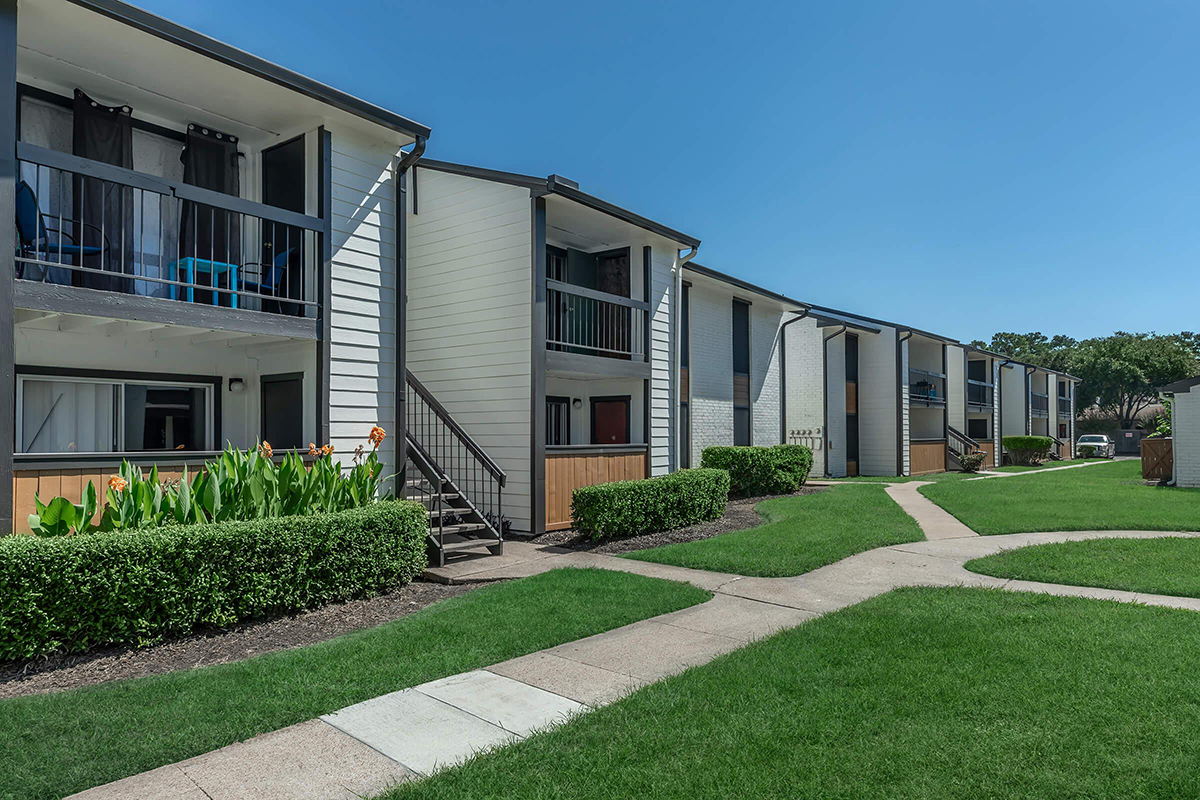A photograph of a two-story apartment community, with a grassy lawn and walkways in the foreground.