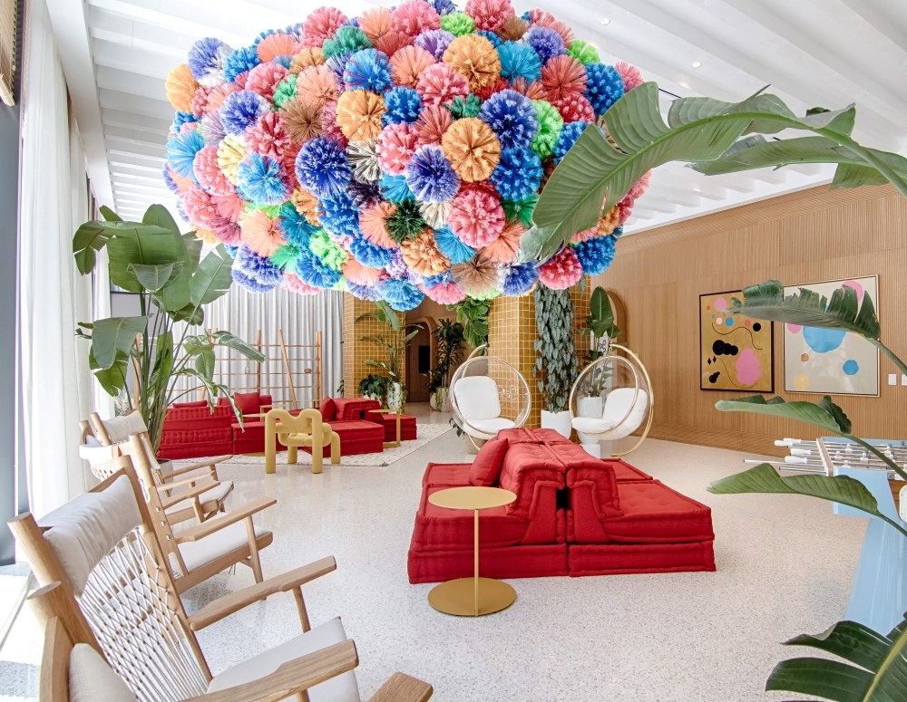 A vibrant flower chandelier hangs from the ceiling in a lobby, showcasing multifamily art in a lively atmosphere.