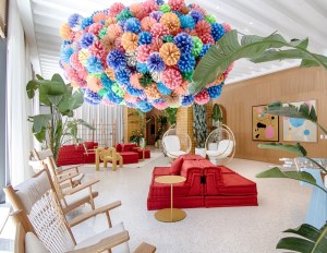 A vibrant flower chandelier hangs from the ceiling in a lobby, showcasing multifamily art in a lively atmosphere.