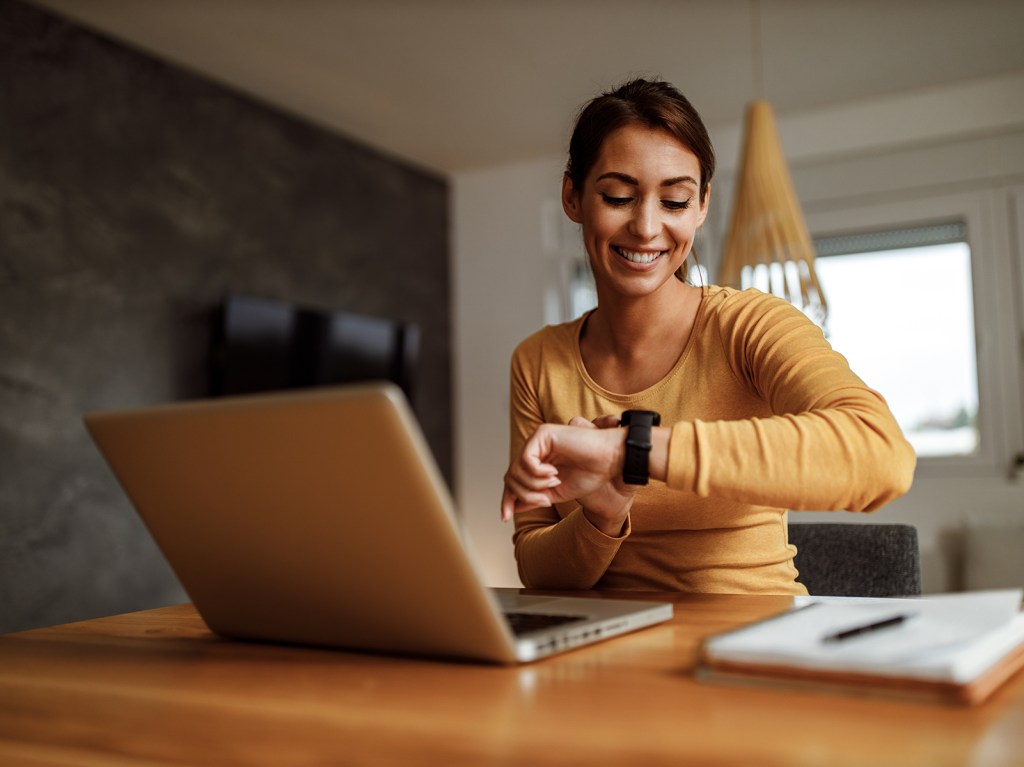 Woman on laptop looking at her watch.