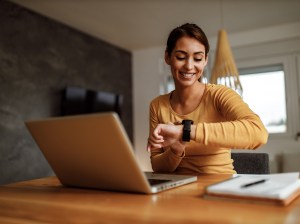 Woman on laptop looking at her watch.