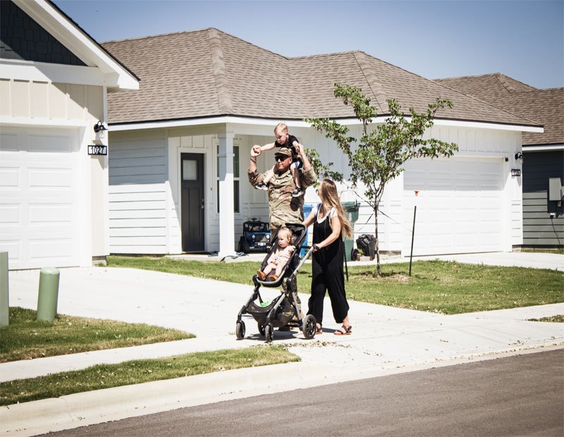 Calvary-Family-Housing military community. Husband and wife walking with a baby in a stroller and a toddler on the husband's shoulders.