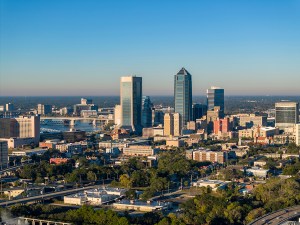 Drone aerial view overlooking downtown Jacksonville, Florida, with the Saint John's River, urban skyline, and waterfront on a clear day.