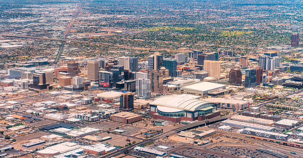 Aerial view of downtown Phoenix, Arizona, with high-rise buildings and a street grid stretching toward hazy mountains.