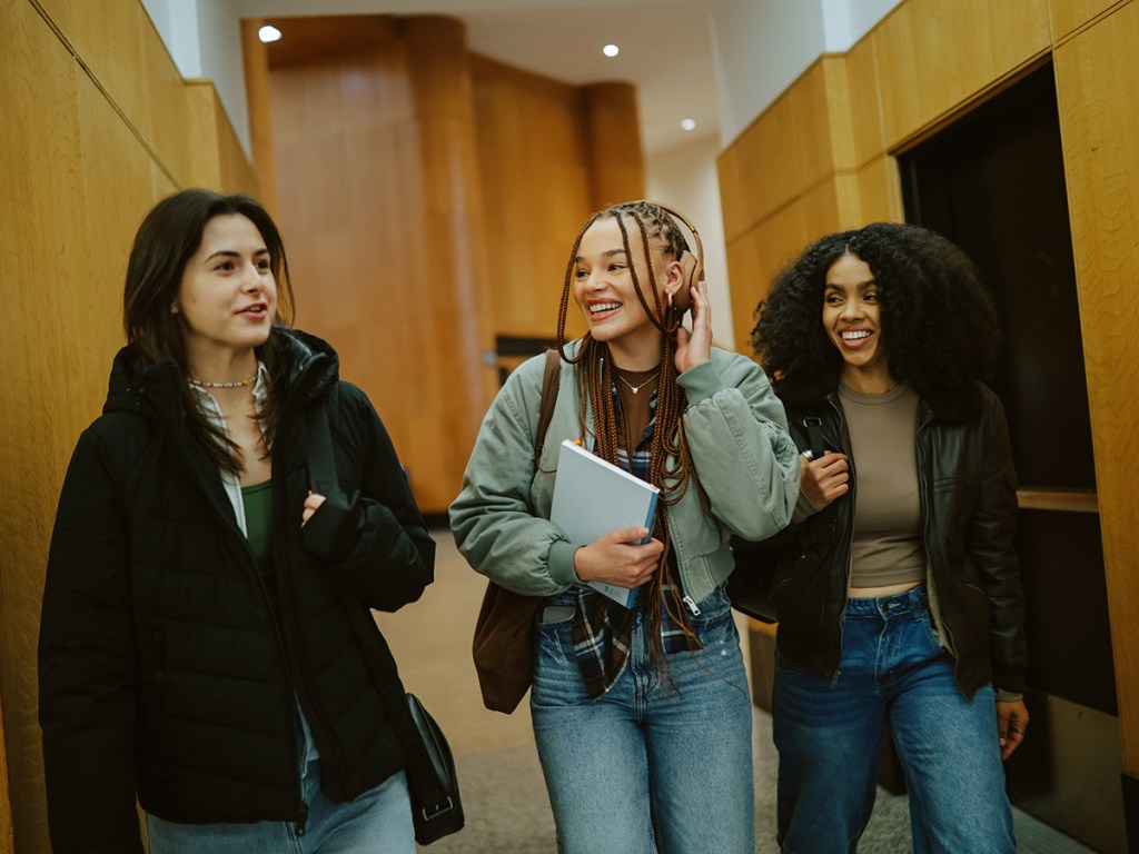 Group of young women arriving at a library or a university in New York, carrying laptops and study materials. Real students preparing to study together as part of everyday student lifestyle.