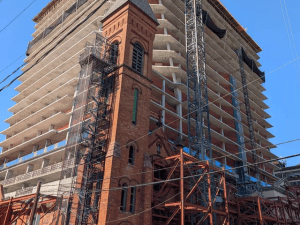 Exterior shot of the redevelopment of the historic St Lucy Church at The Lucy, as well as the vertical construction of a 24-story glass tower behind the church.